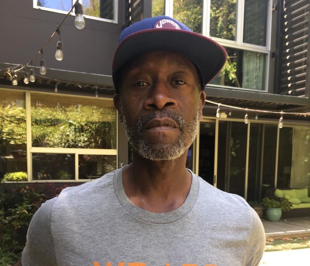 Don Cheadle is wearing a cap and gray tee