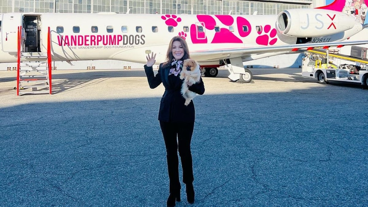 Lisa, adorned in a black suit and pants, poses with her dog against the backdrop of a plane.