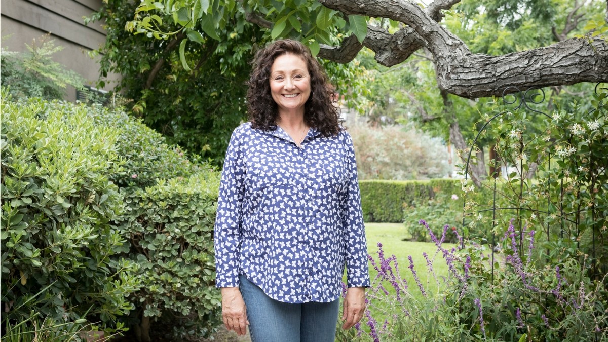 Debbie Pollack standing with blue t shirt and jeans in front of greenery